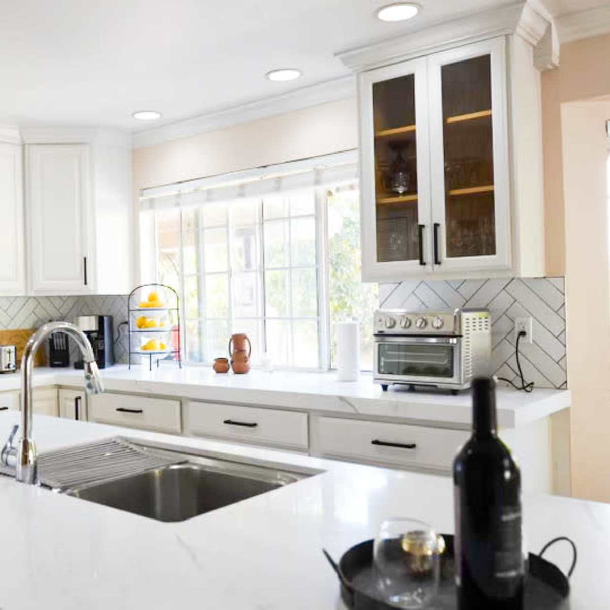 A modern kitchen with white cabinetry, a large island with a sink, and a herringbone-patterned backsplash.