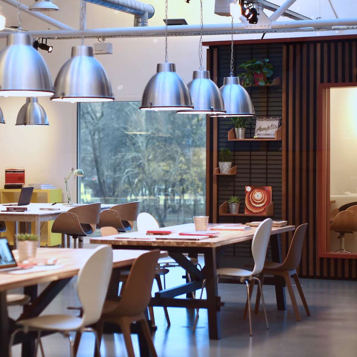 A modern office space with wooden tables, stylish chairs, and large pendant lights hanging from the ceiling.