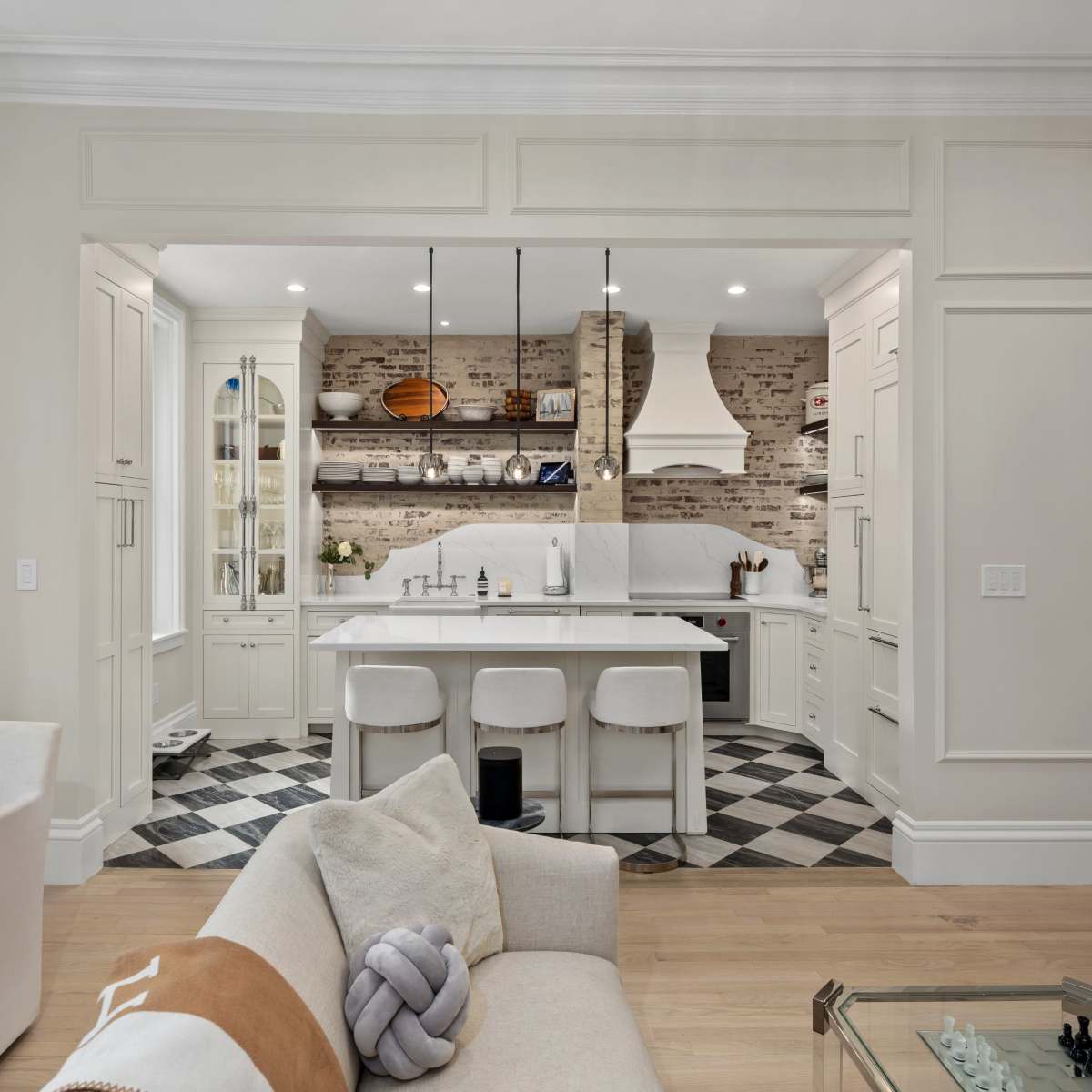 A modern kitchen features a large island with bar stools, surrounded by light-colored cabinetry and a brick backsplash.