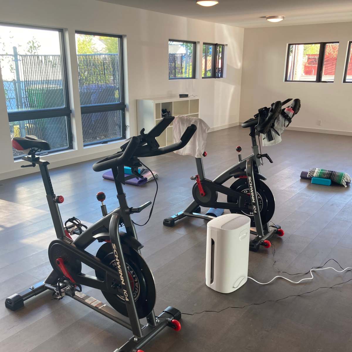 A fitness room with two stationary bicycles, a portable air purifier, and some workout mats on the floor.