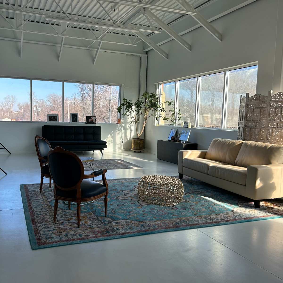 A bright, modern interior space with a black sofa, a beige couch, and large windows letting in natural light.