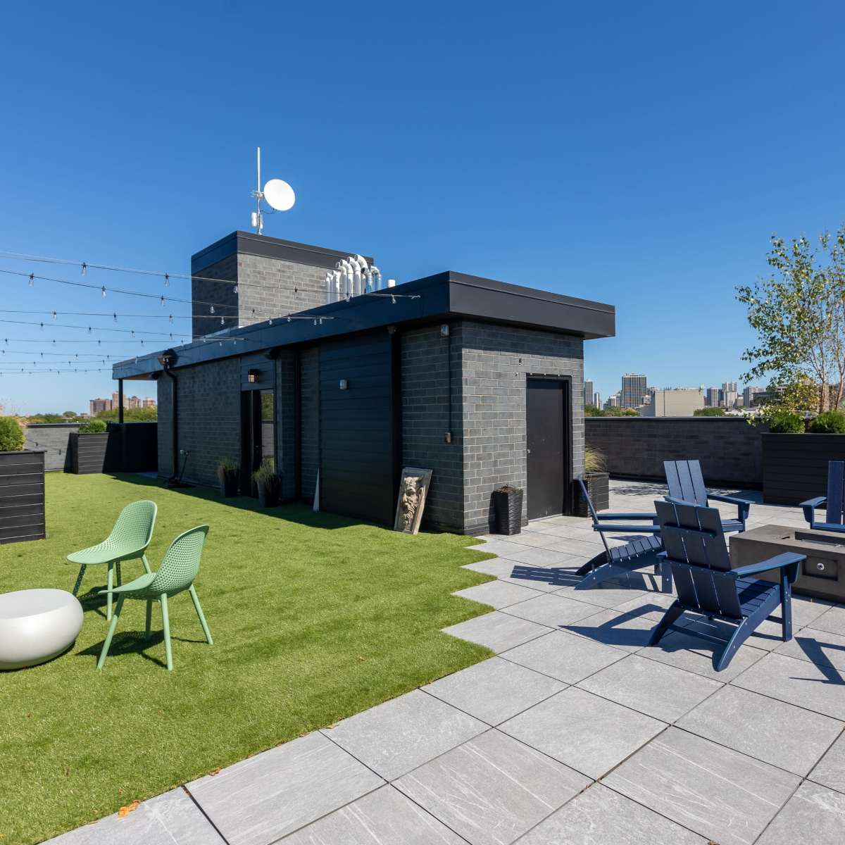 A rooftop area with green grass, seating arrangements, and a view of a city skyline.
