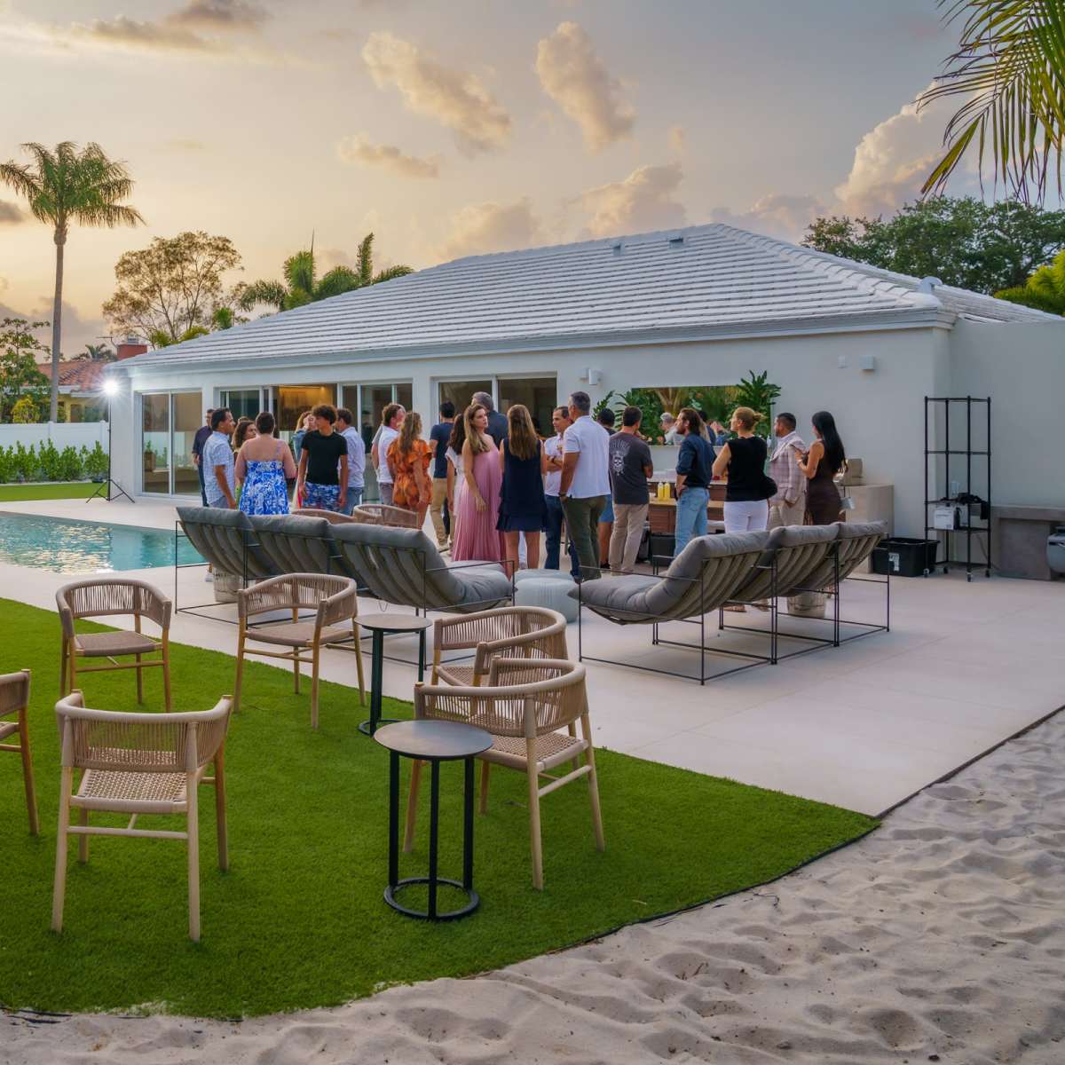 A group of people socializes around a swimming pool in a backyard setting during sunset.