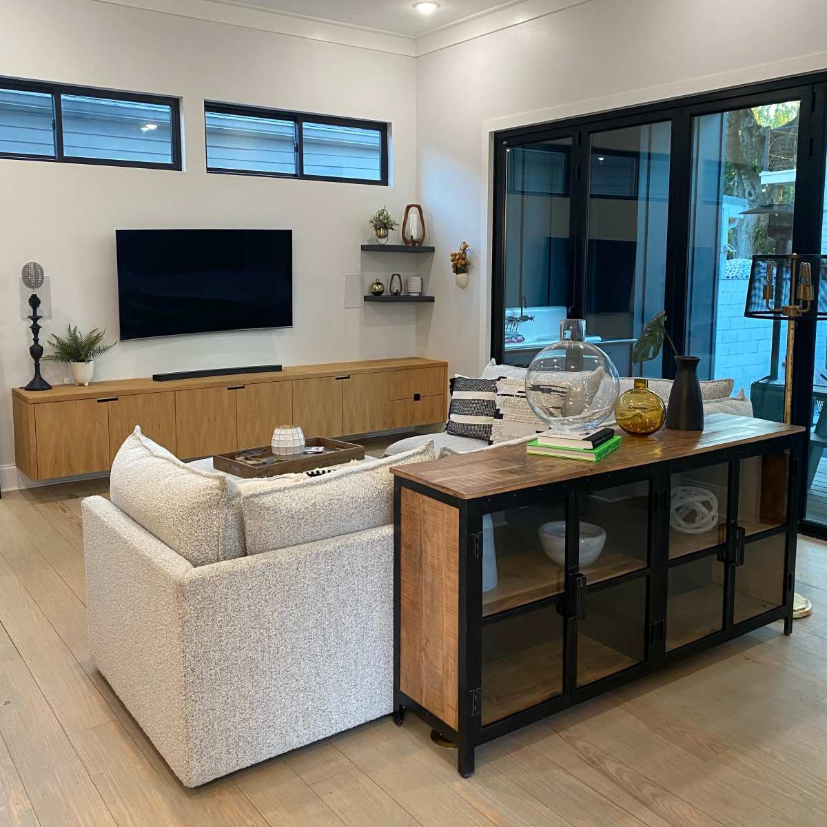 A modern living room with a white sofa, a wooden sideboard, and large windows that provide natural light.