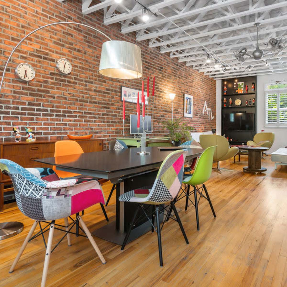 A spacious, modern interior featuring a dining area with colorful chairs, a wooden table, and exposed brick walls.