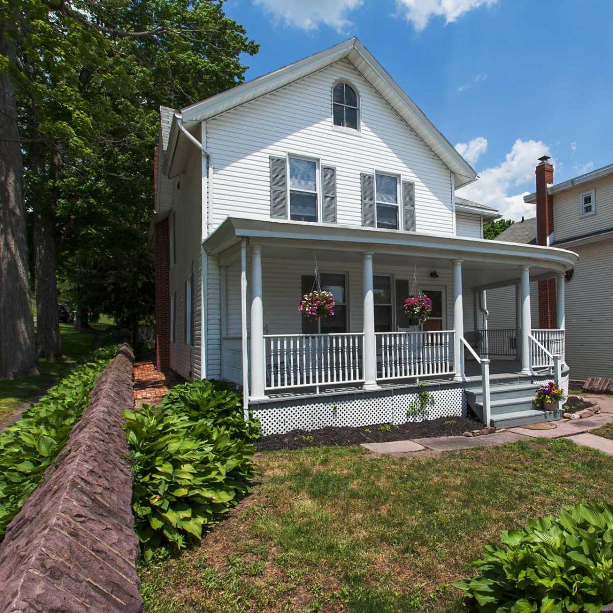 A two-story white house with a front porch, surrounded by a grassy lawn and a low stone wall.