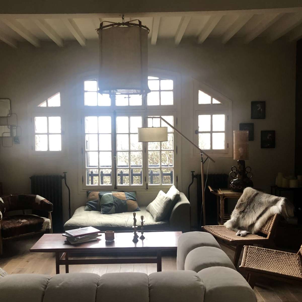 A cozy living room features a mix of seating, large windows, and a wooden coffee table.