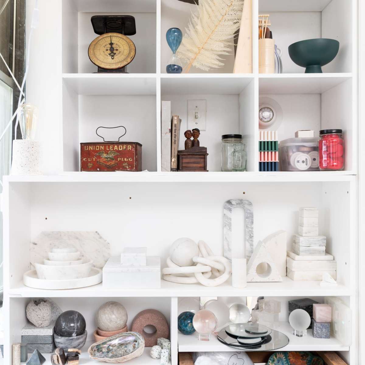 A white shelving unit filled with a variety of decorative objects, containers, and glassware, arranged neatly across several compartments.