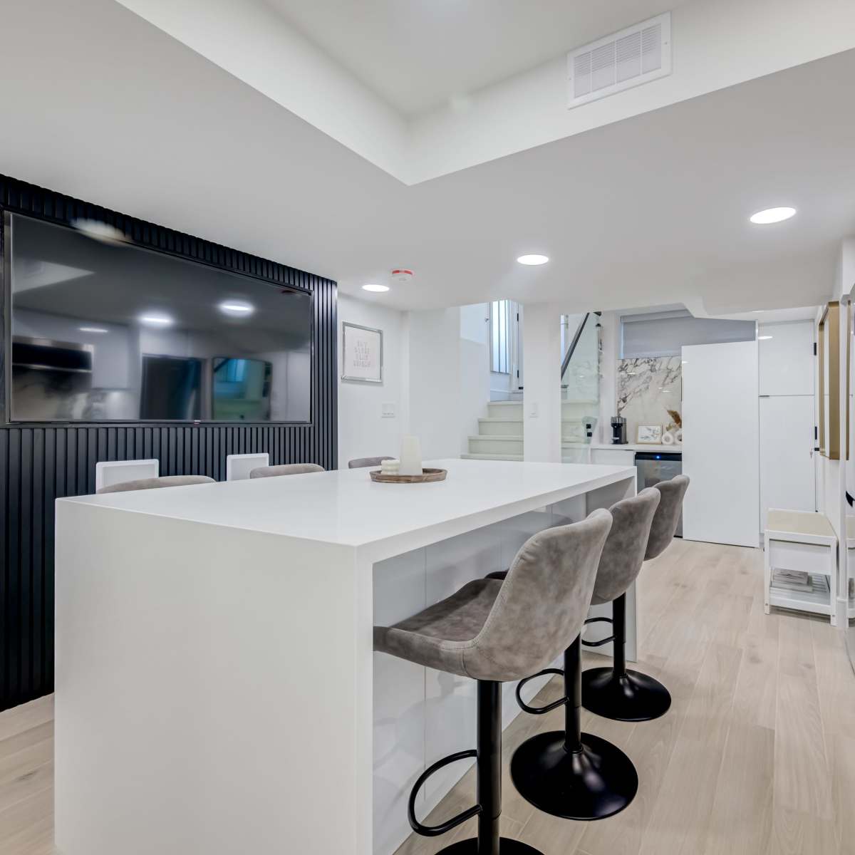A modern kitchen features a large island with bar stools, sleek appliances, and a wall-mounted TV.