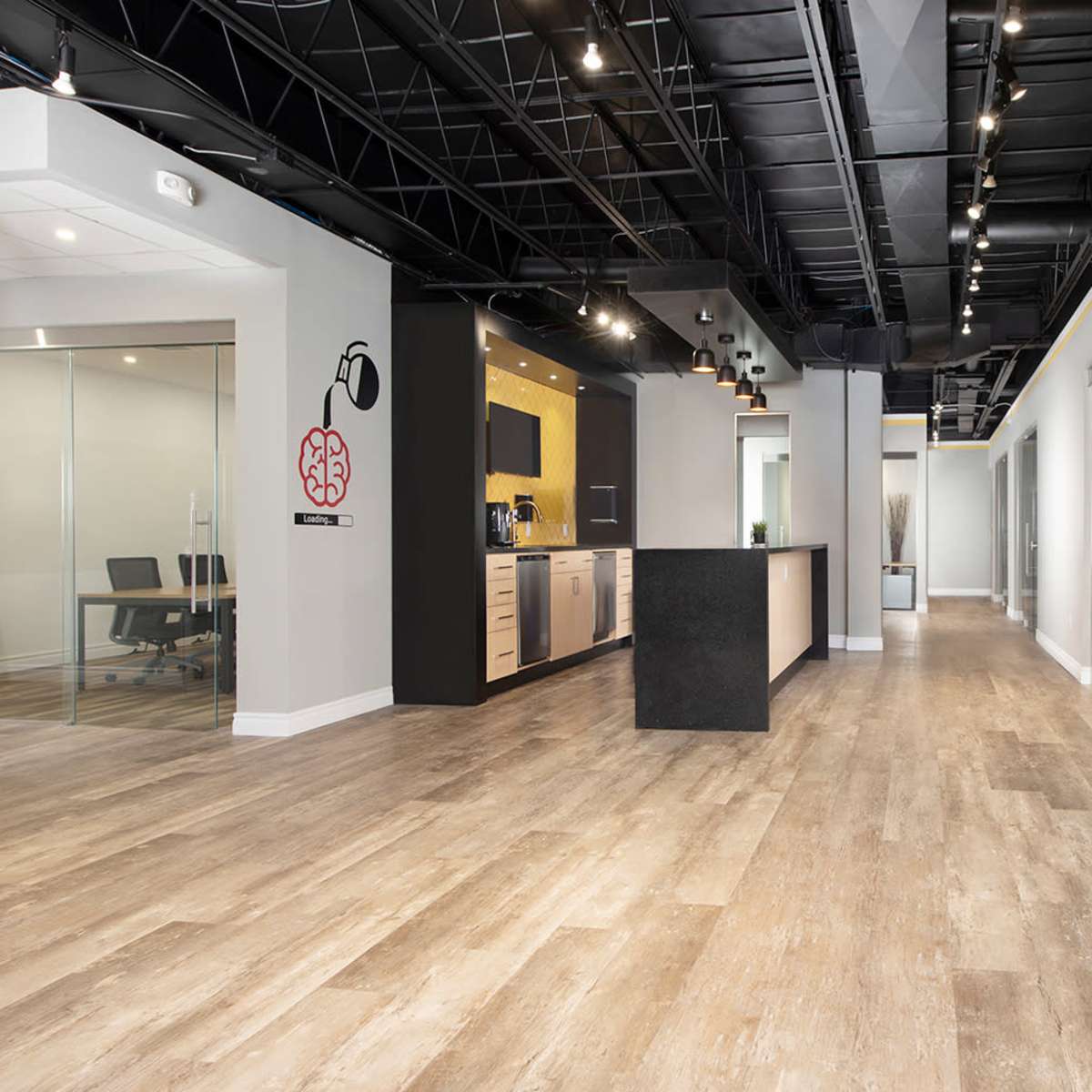 A modern office interior with a central dark island counter, glass-walled meeting rooms, and wooden flooring.