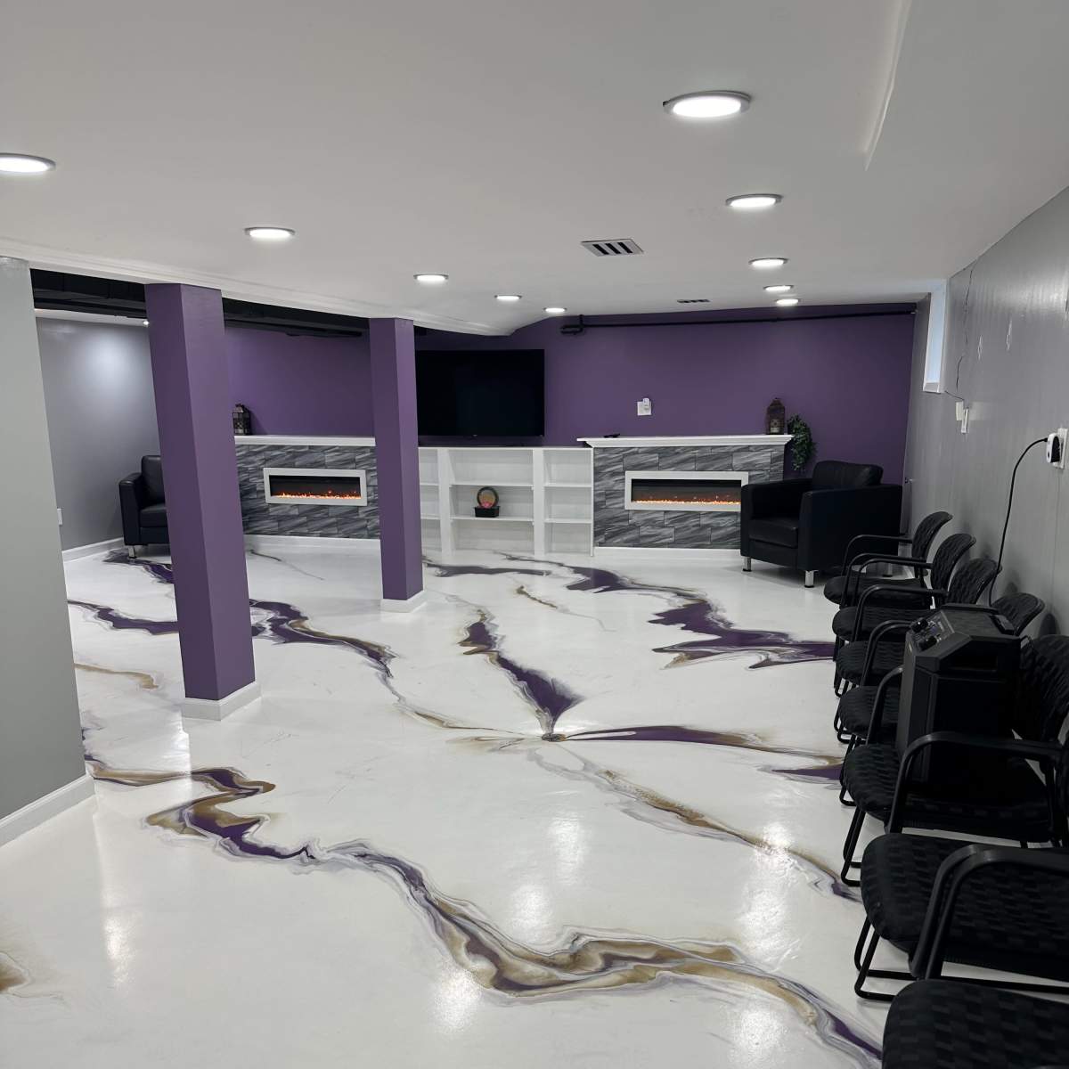A modern interior space with purple walls, a white floor featuring a marbled pattern, and seating arranged in front of a television and electric fireplace.