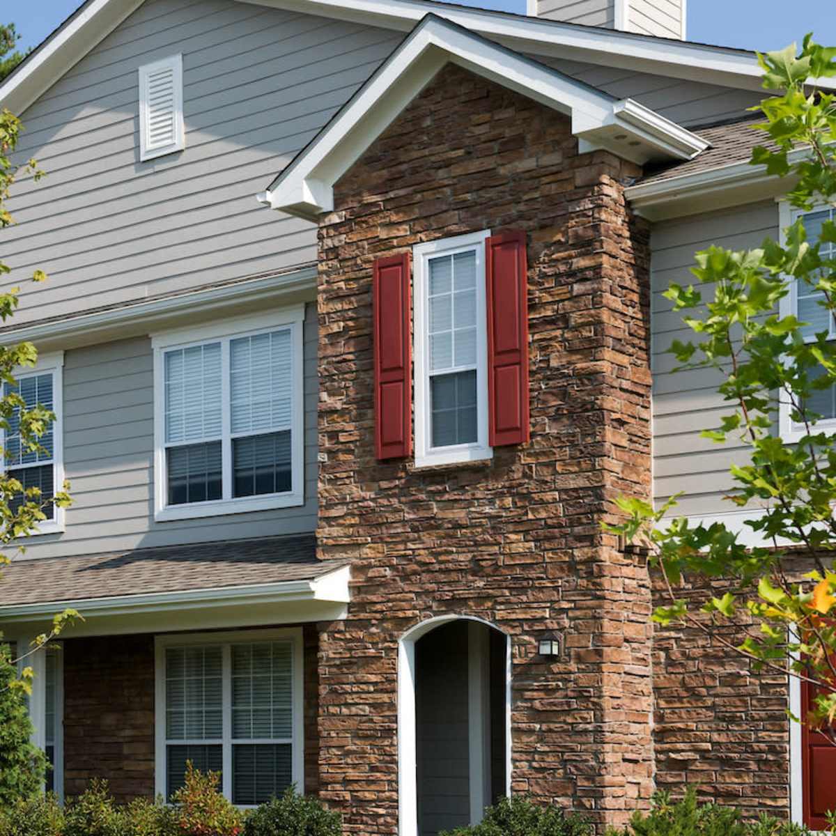 A two-story house featuring a stone facade, red shutters, and a landscaped front yard.