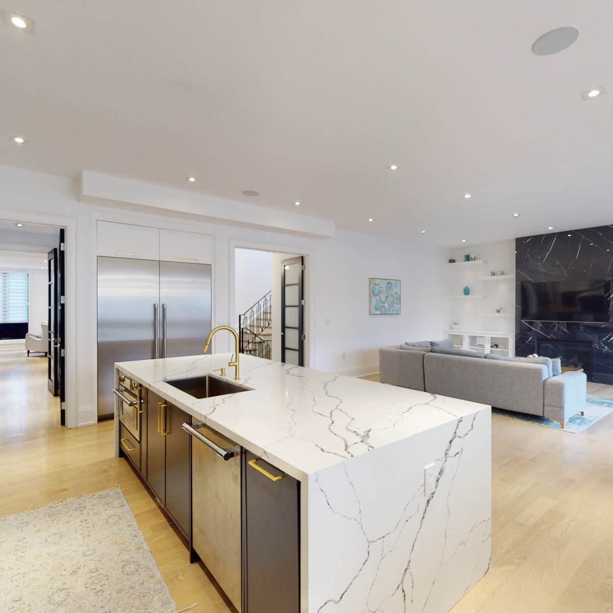 A modern kitchen with a central island, stainless steel appliances, and a connected living area featuring a couch and a large flat-screen TV.