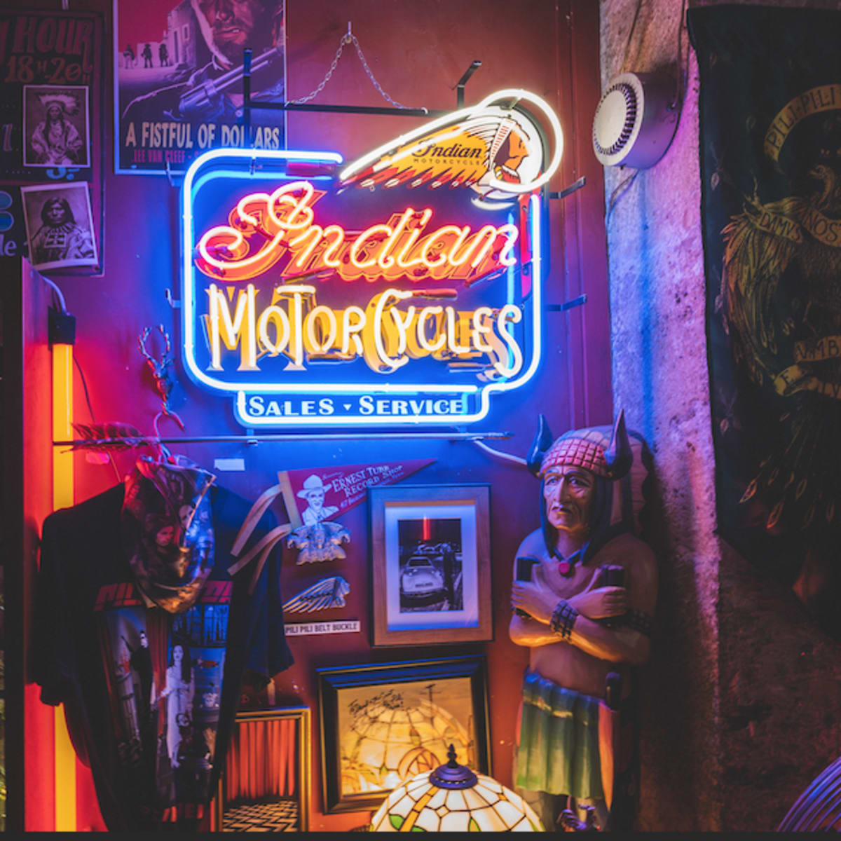 A neon sign for "Indian Motorcycles" illuminated against a backdrop of various collectibles and merchandise, including a statue of a Native American.