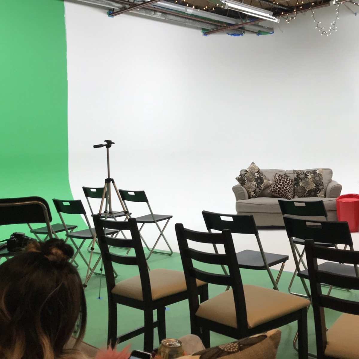 A studio setup with two sofas, several black chairs arranged in rows, a microphone stand, and a green-screen wall on one side.