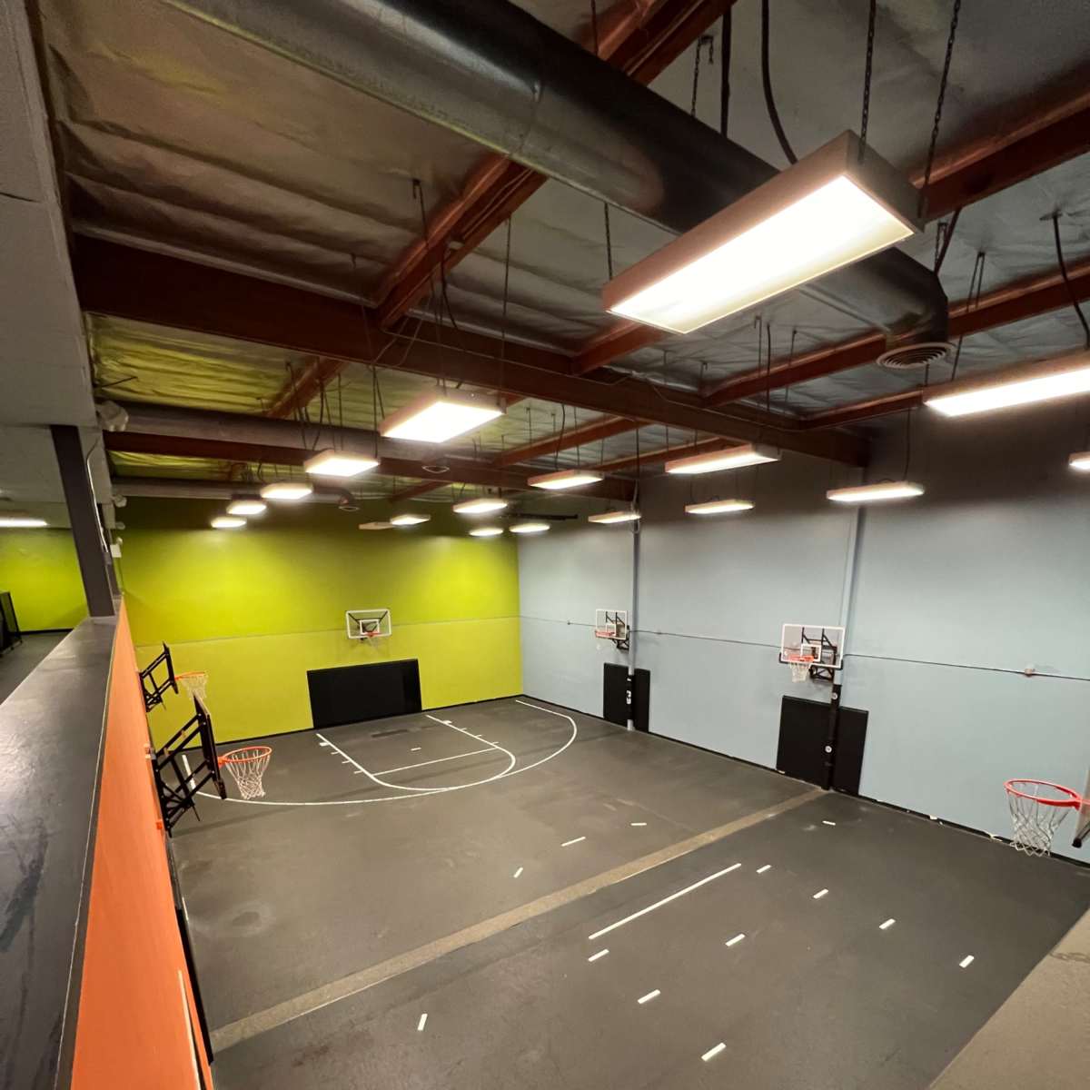 A spacious indoor basketball court with two hoops, a green and gray color scheme on the walls, and marked floor lines.