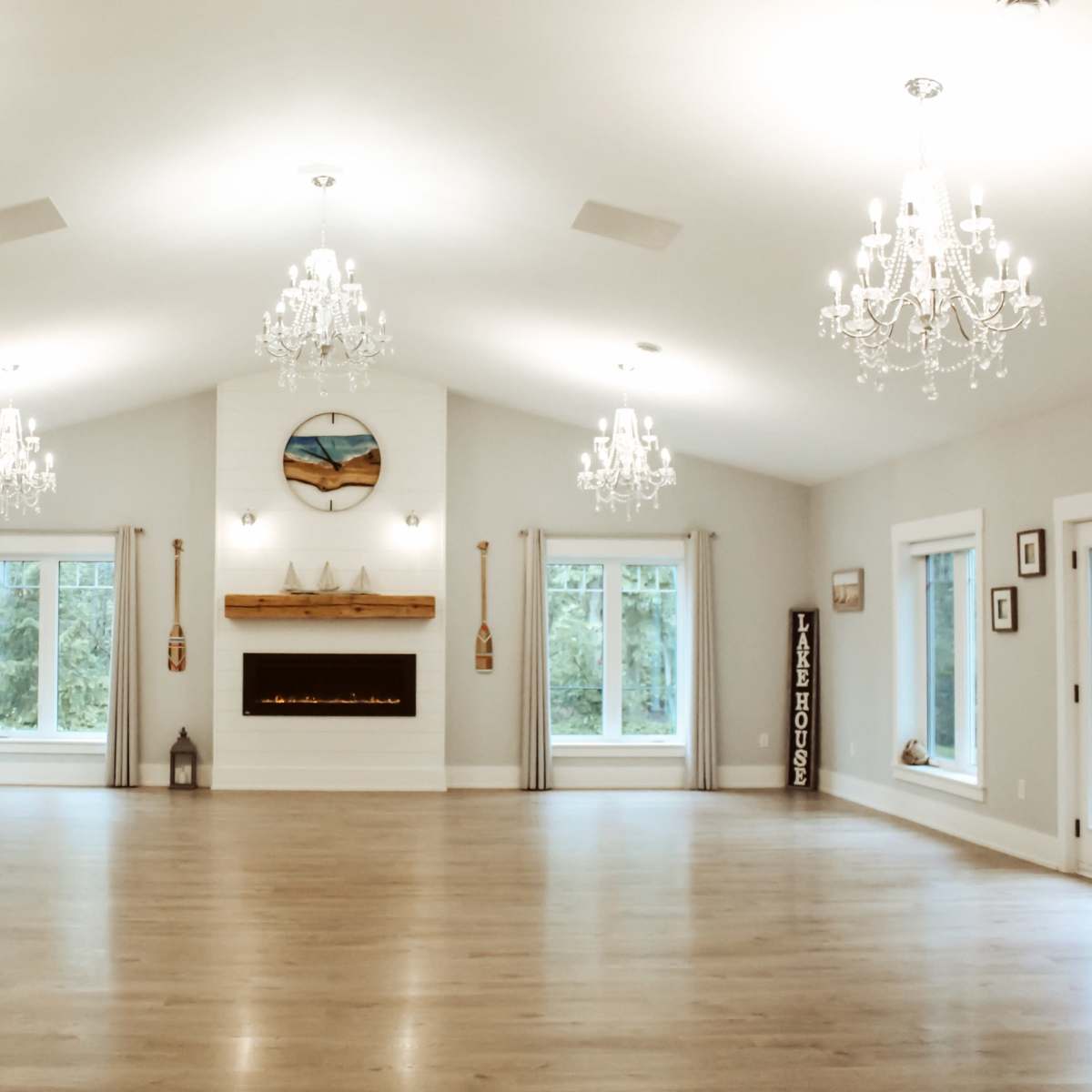 A spacious interior room with a polished wooden floor, large windows, and several crystal chandeliers hanging from the ceiling.