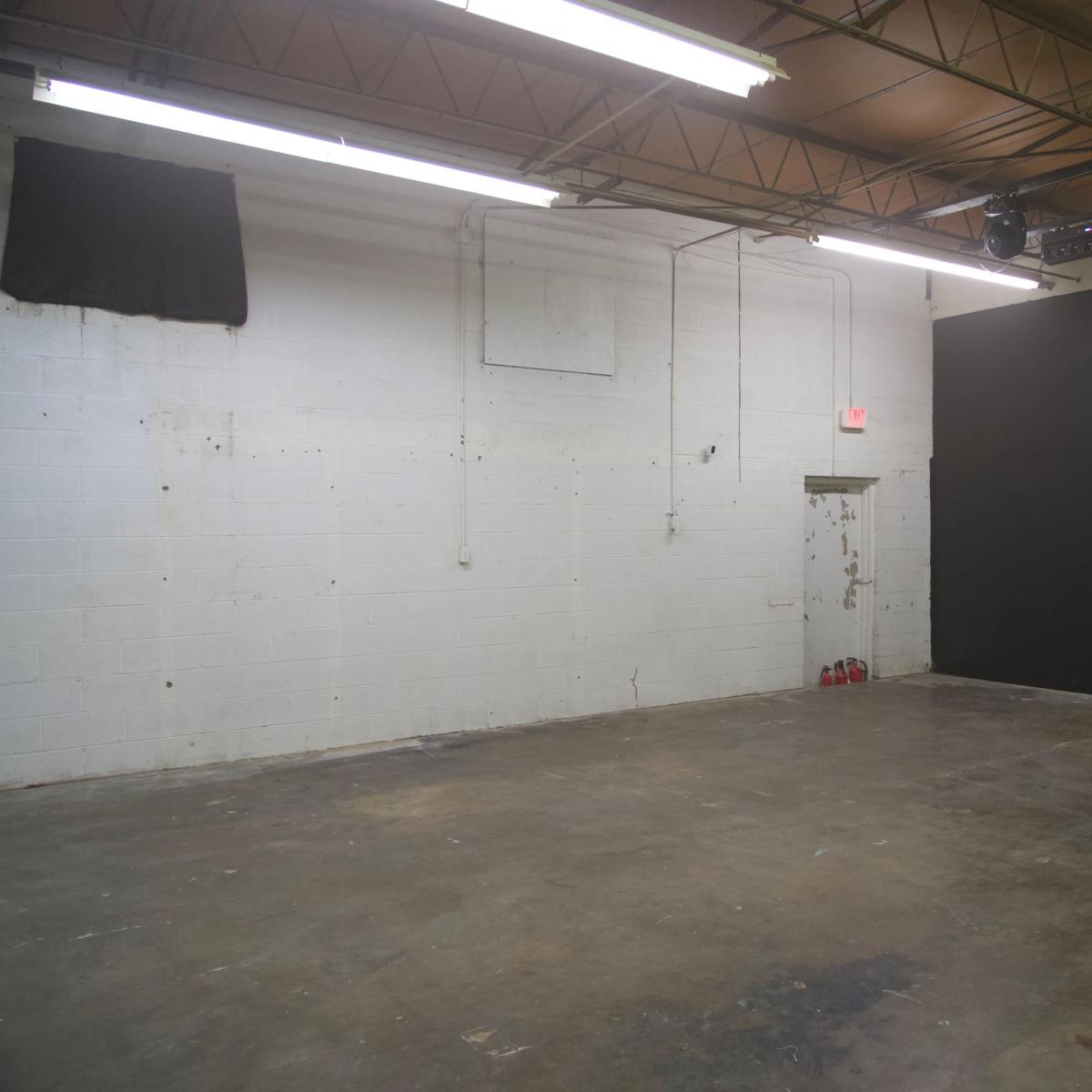 An empty room with a concrete floor, white walls, and a large black wall at one end.