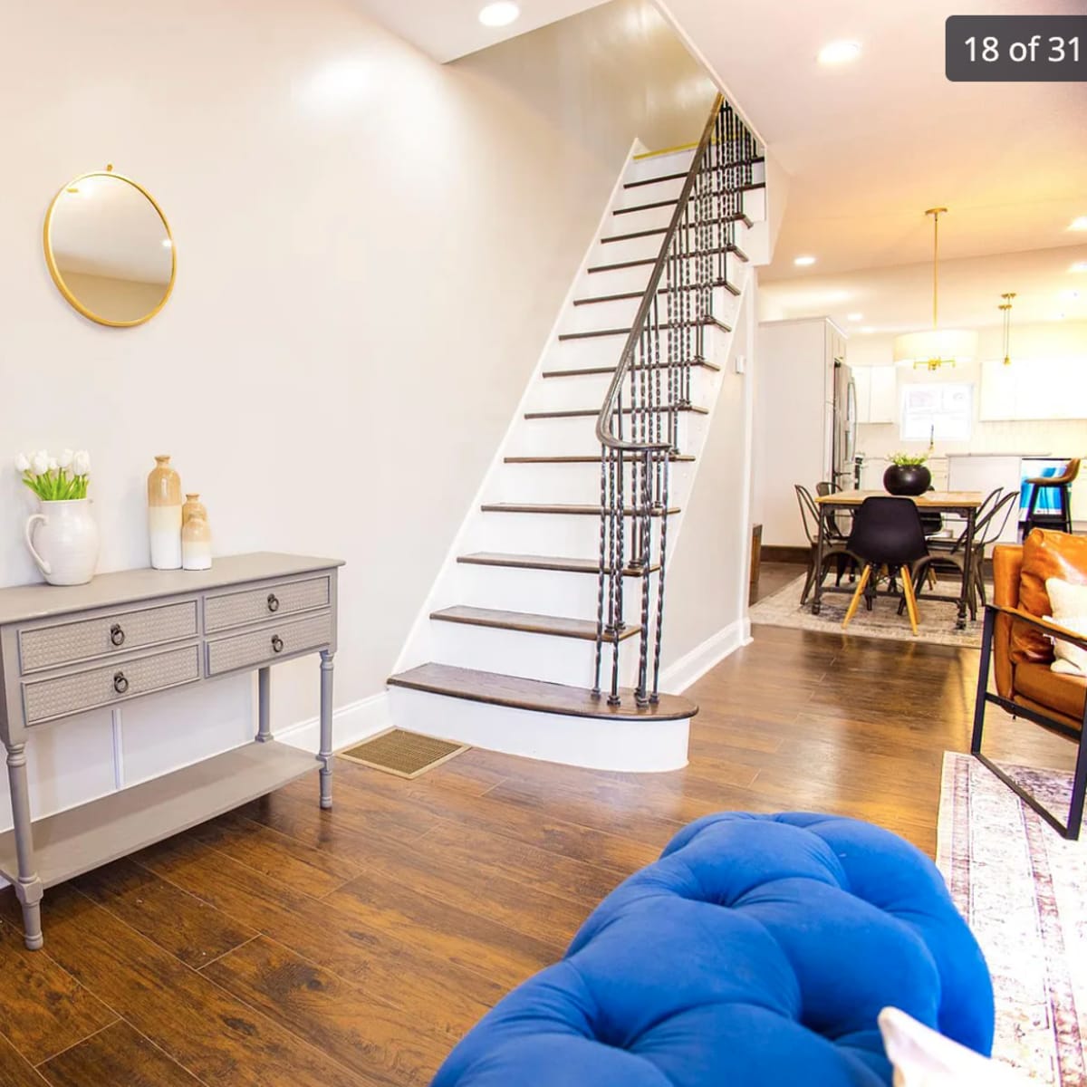 A hallway with a brick accent wall, a circular mirror above a gray console table, and a staircase leading to the upper floor.