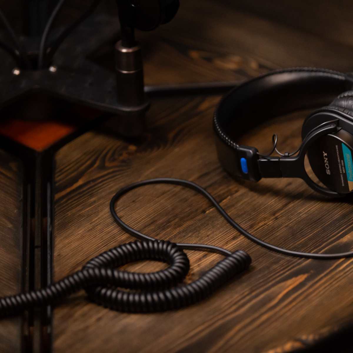 A pair of black Sony headphones rests on a wooden table, connected by a coiled cable.