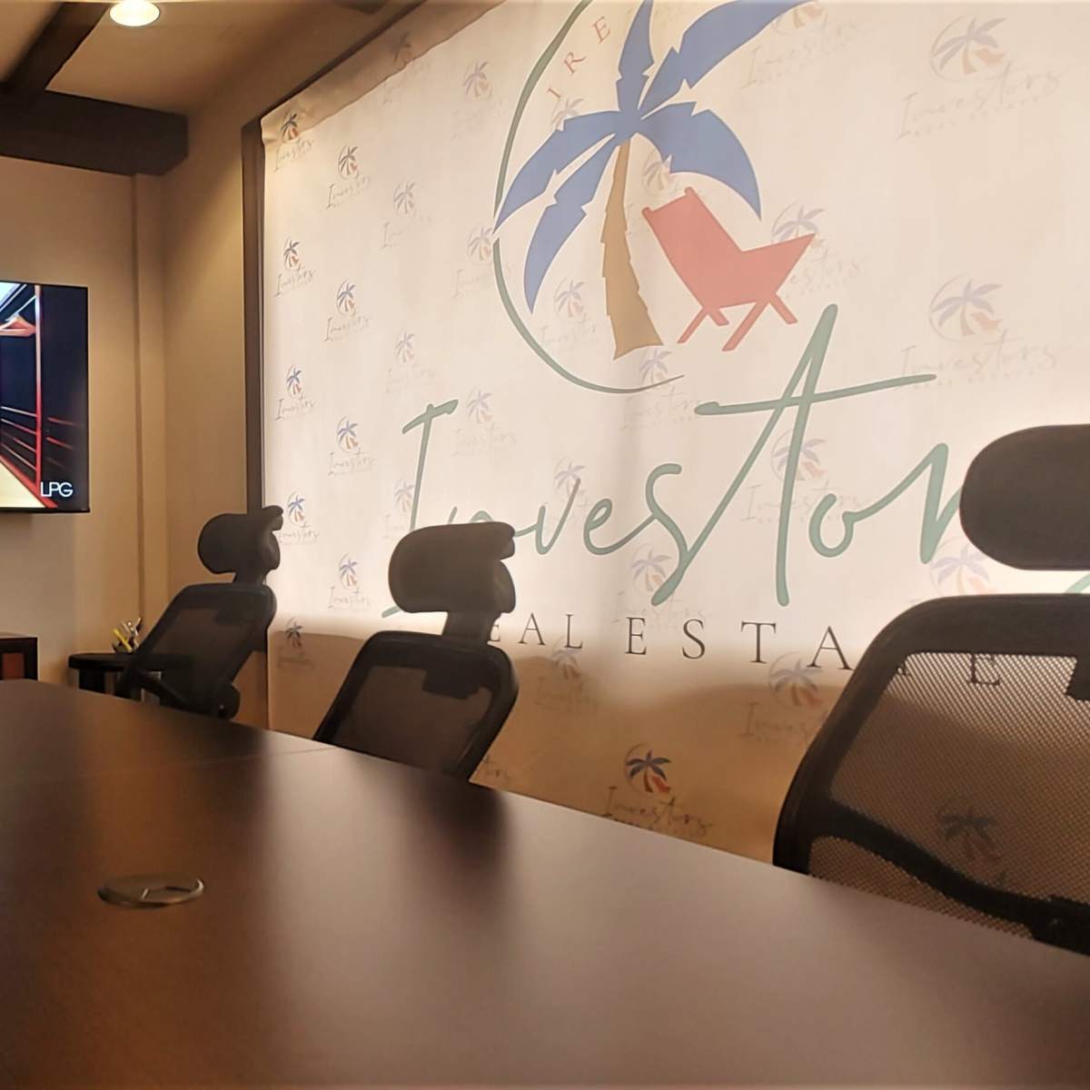A conference room with a large screen displaying a room interior, surrounded by several ergonomic chairs and a decorative wall featuring a company logo.