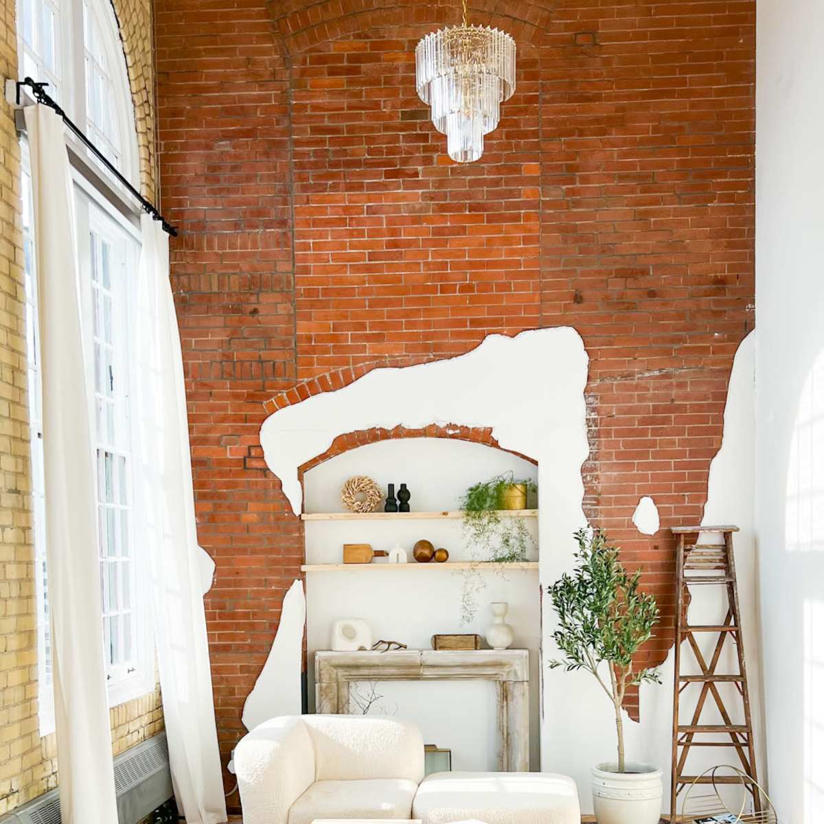 A stylish living room featuring a brick wall with a white-painted section, a bookshelf with decorative items, a potted plant, and a plush, pink seating area.
