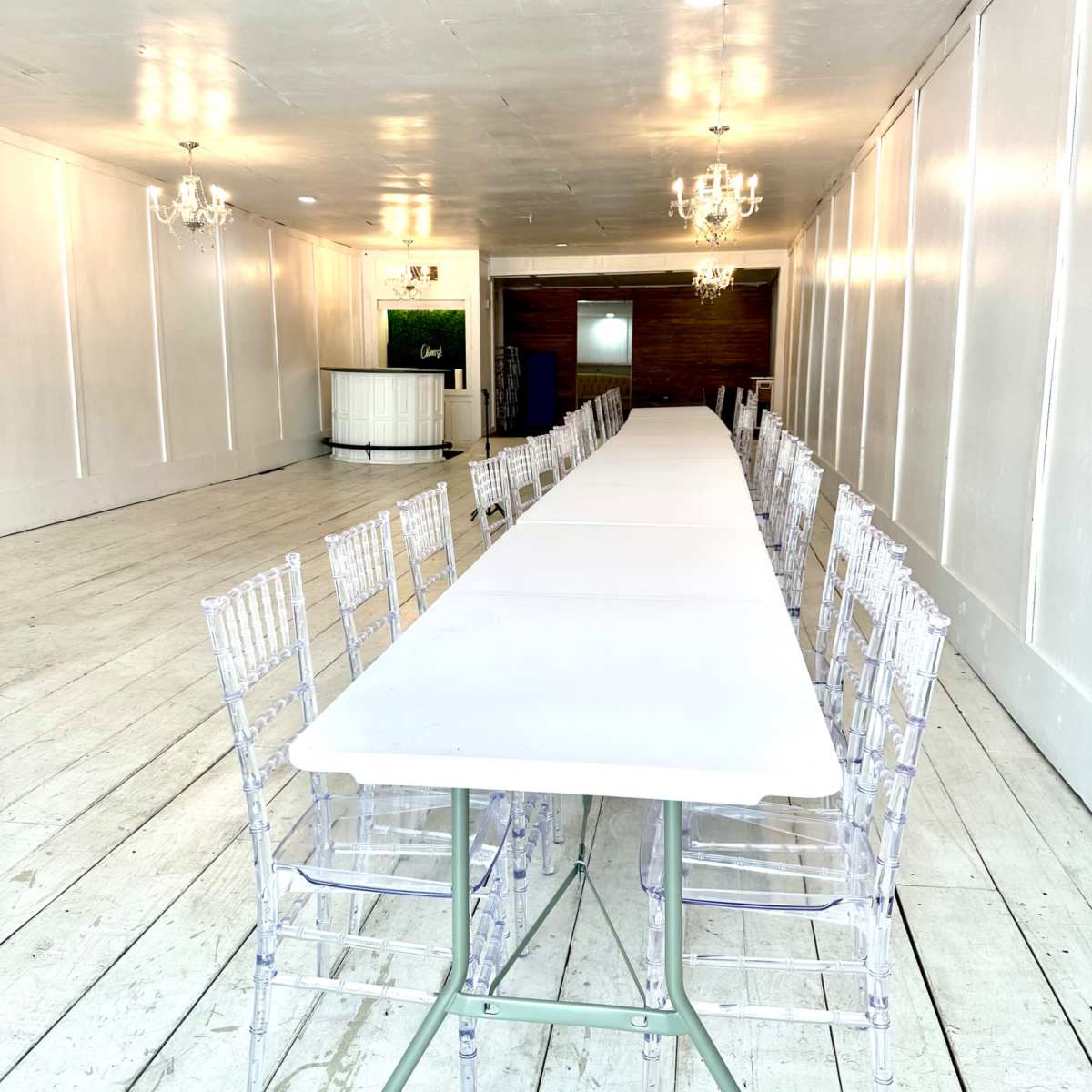 A long, white table is set up in a spacious room with chandeliers and wooden accents.
