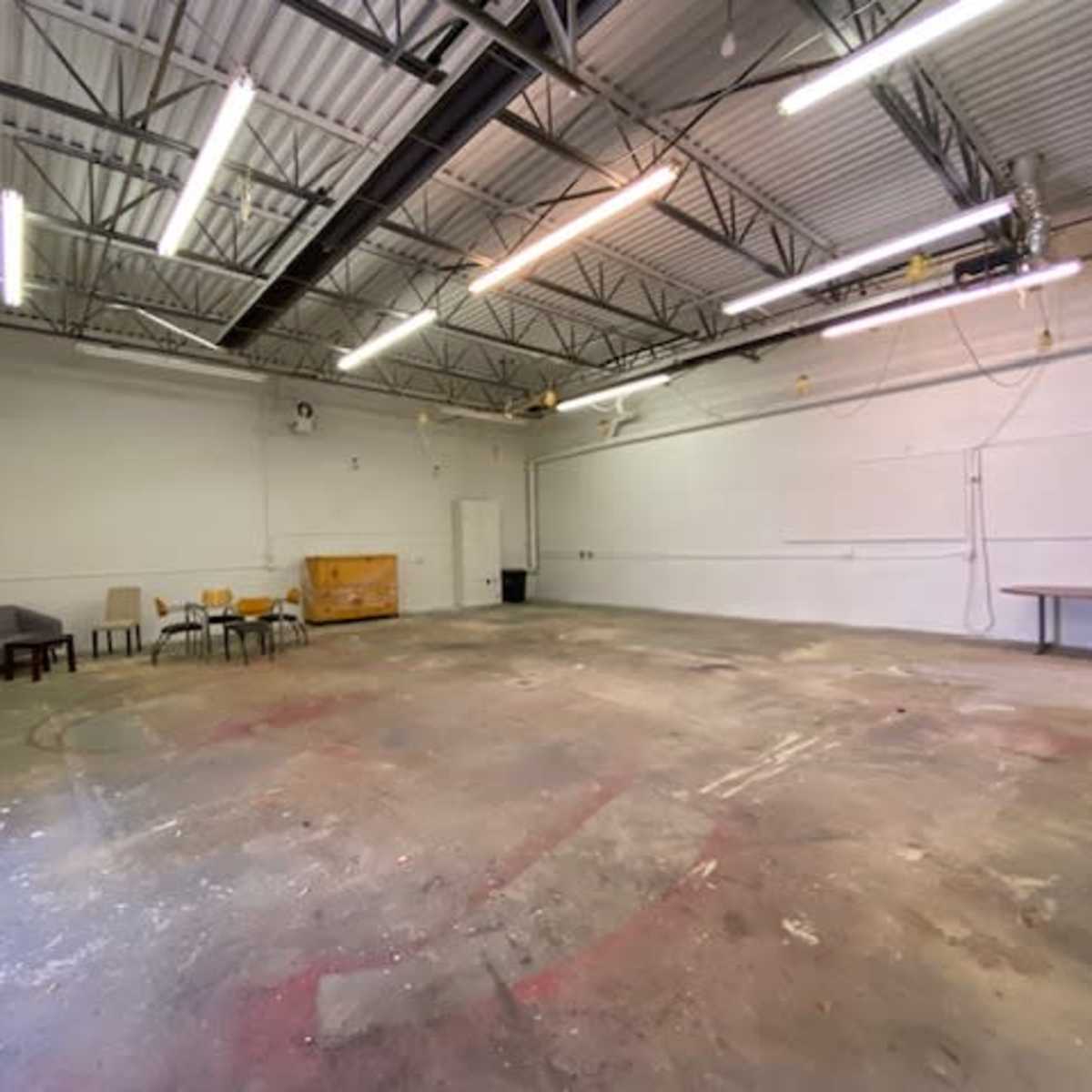 A spacious, unfinished room with a concrete floor, scattered furniture, and overhead lighting.
