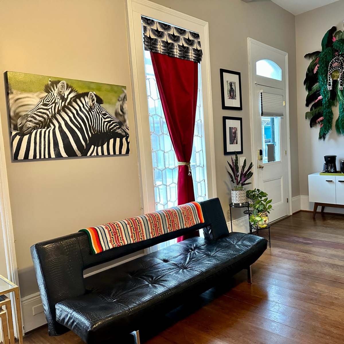 A cozy living area featuring a black bench, a zebra-striped artwork on the wall, a red curtain, and a white furniture set with a small refrigerator and coffee maker.