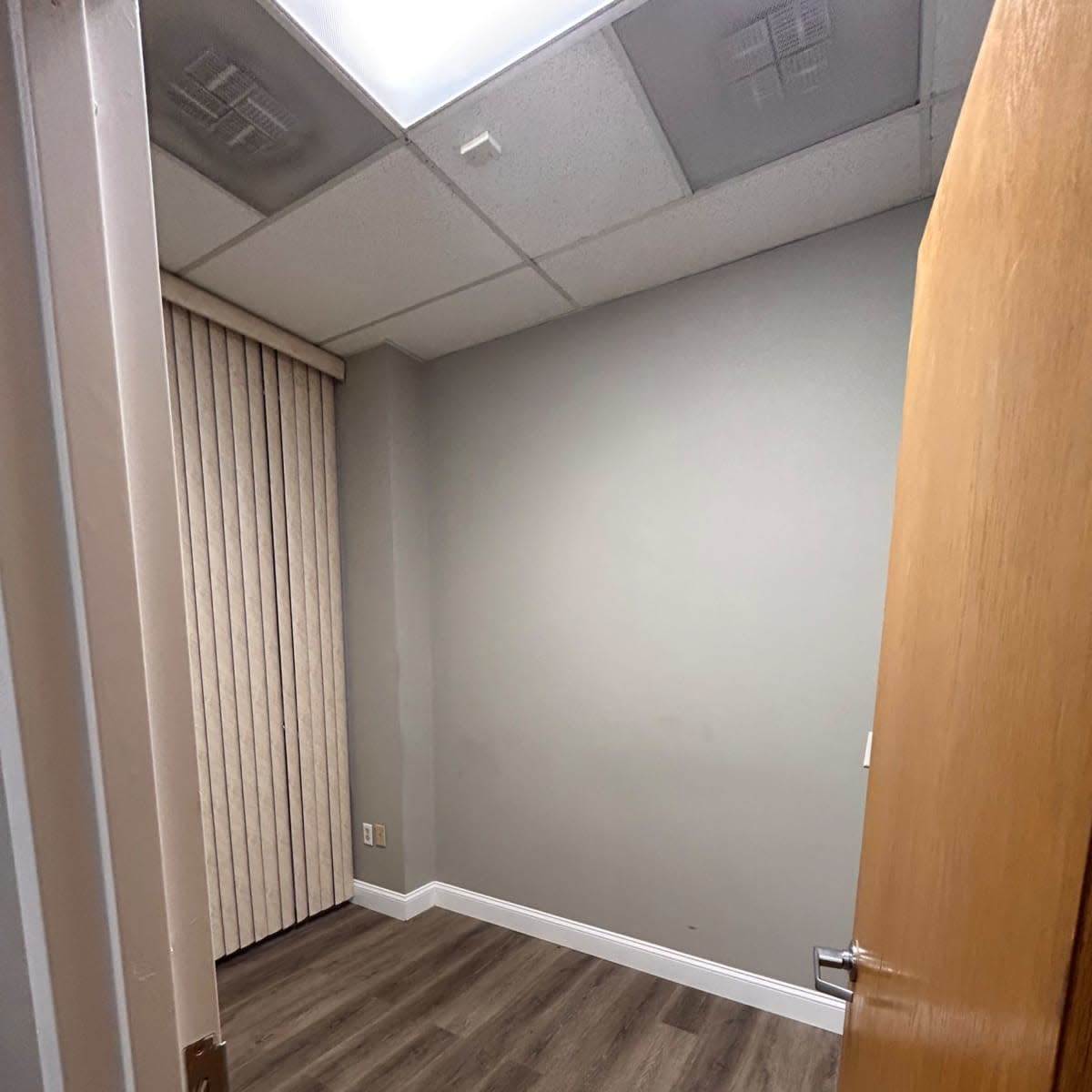 An empty room with beige walls, wooden flooring, and a door partially open.