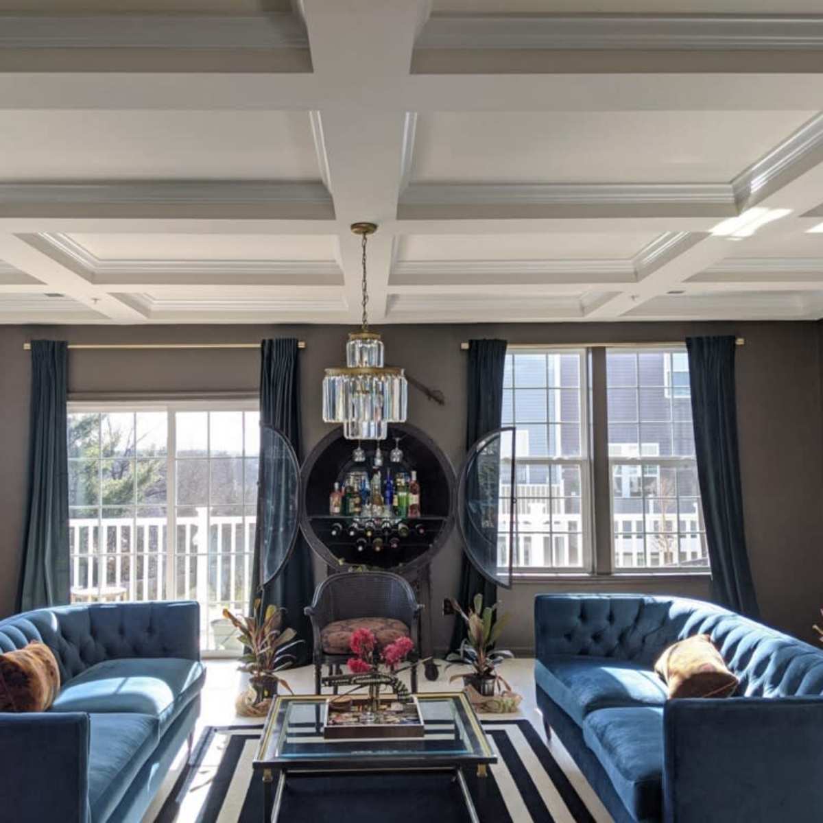 A modern living room featuring two blue sofas facing each other, a glass coffee table with a decorative arrangement, and large windows with sheer curtains.