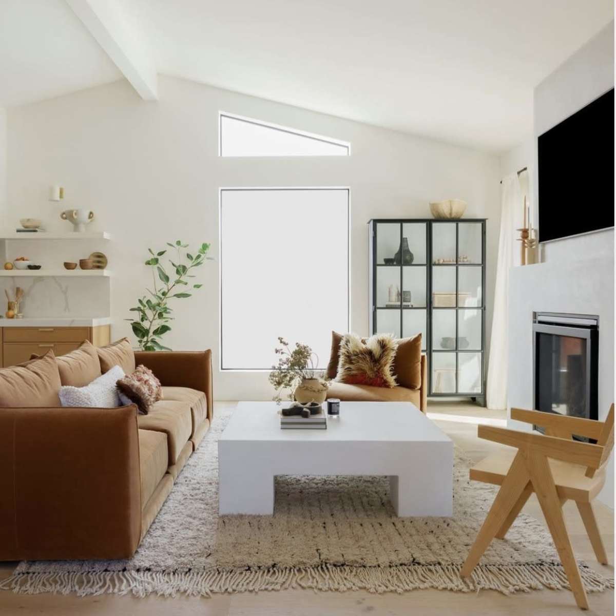 A modern living room features a light-colored sofa, a minimalist coffee table, a glass display cabinet, and a fireplace.