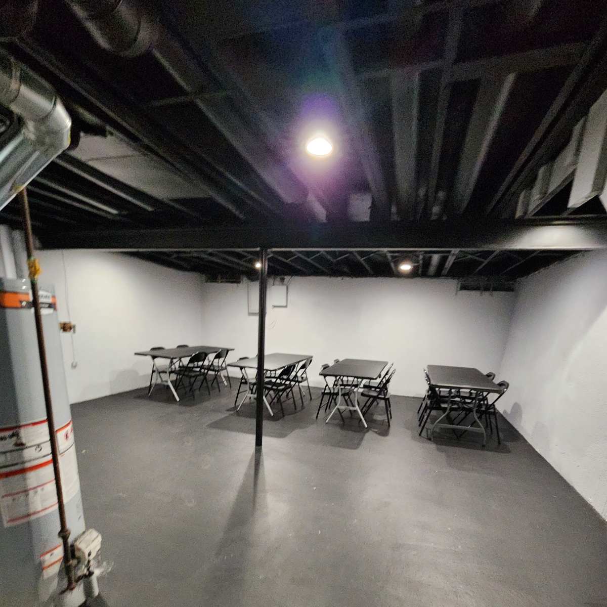 A dimly lit basement space featuring several folding tables arranged in rows on a concrete floor.