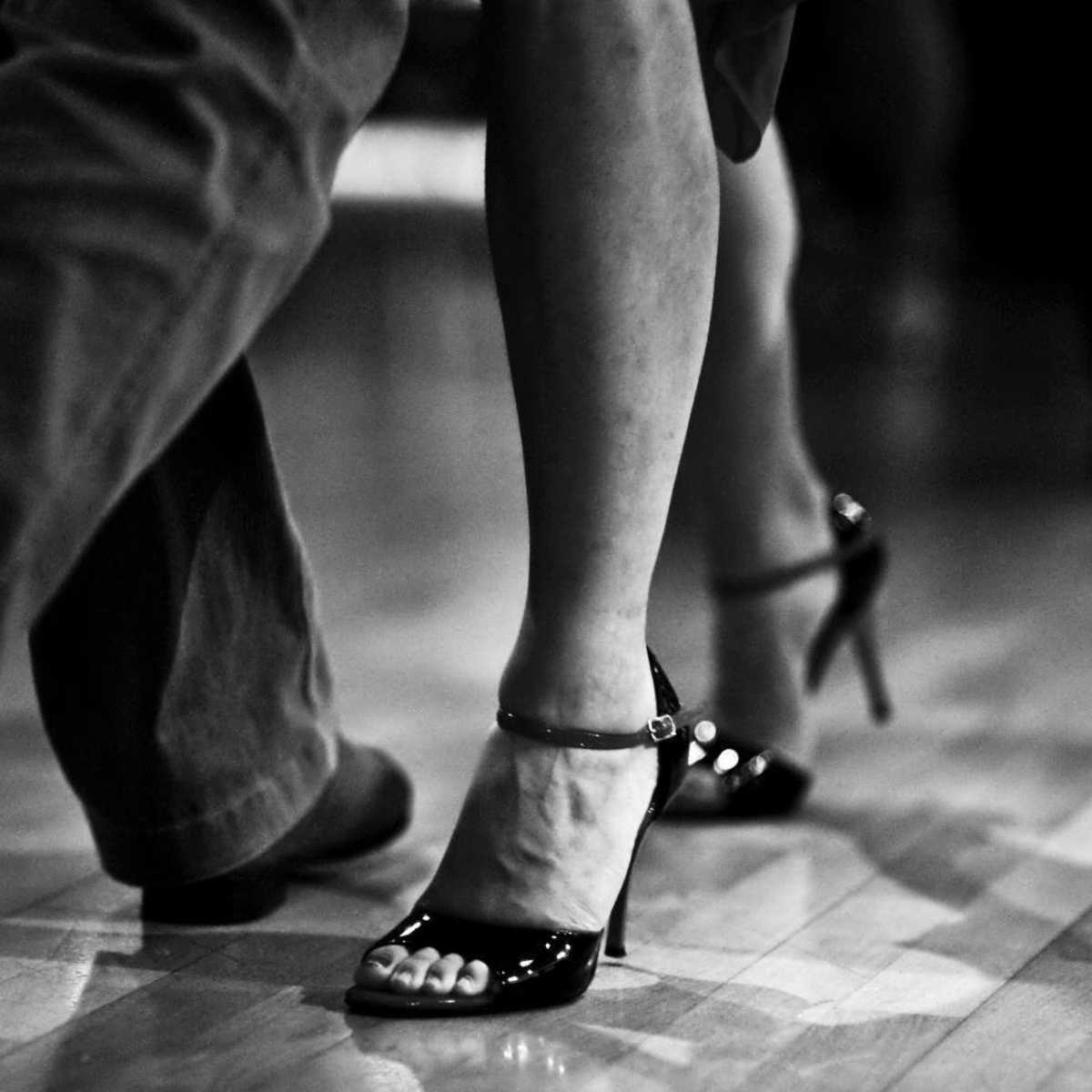 A close-up of two pairs of feet engaged in dancing on a wooden floor.