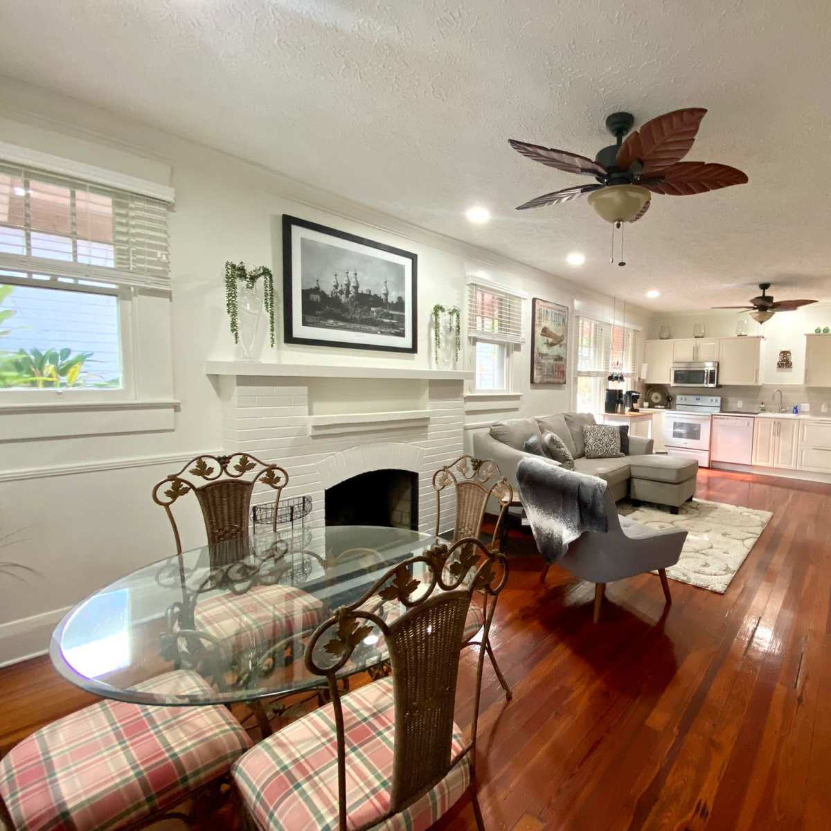 A well-lit living area featuring a dining table with four chairs, a sofa, and a kitchenette with modern appliances.