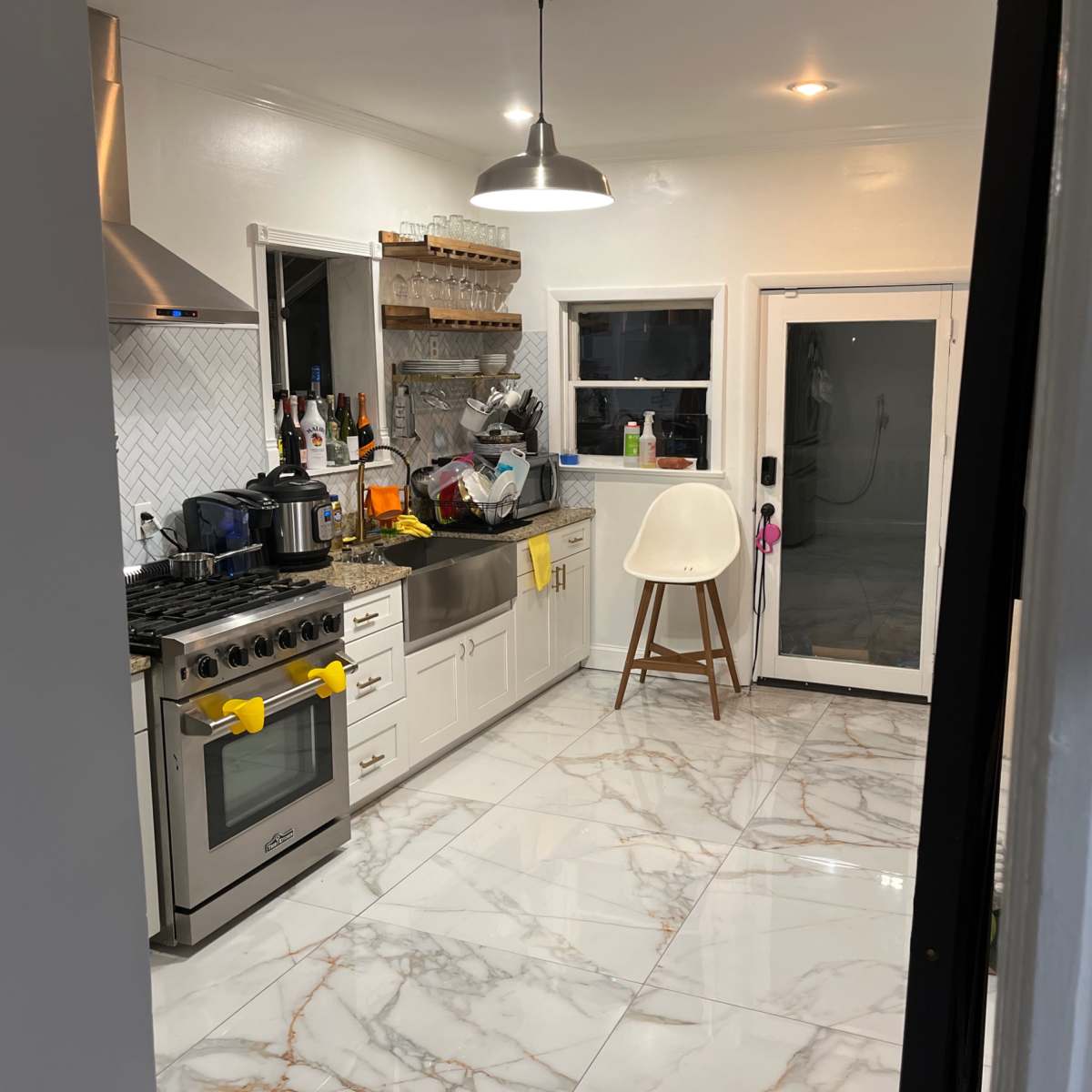 A modern kitchen features a large island, stainless steel appliances, and marble flooring with a view of a glass door leading to an outdoor space.