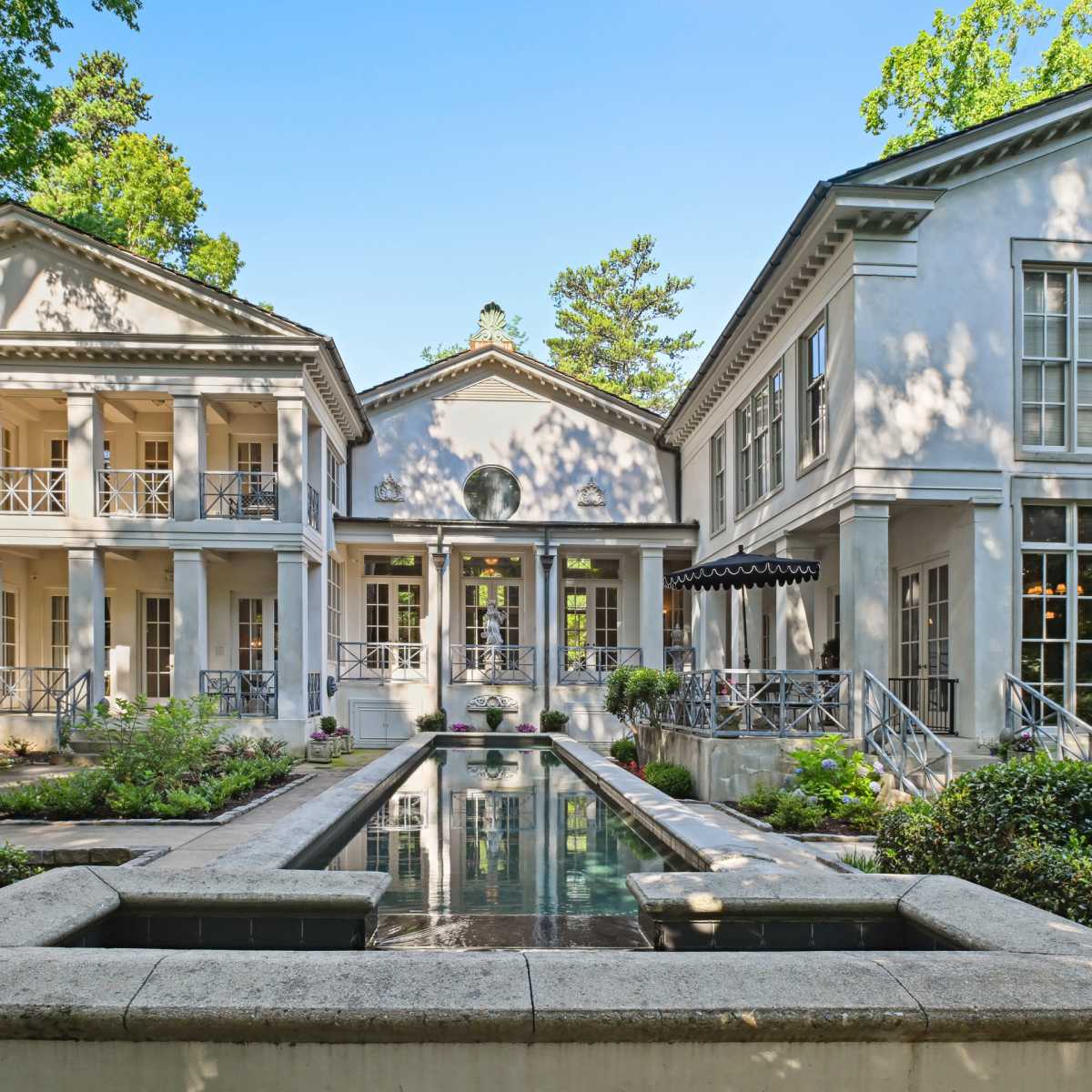 A spacious, modern house with symmetrical architecture, featuring a central courtyard with a reflecting pool and lush landscaping.