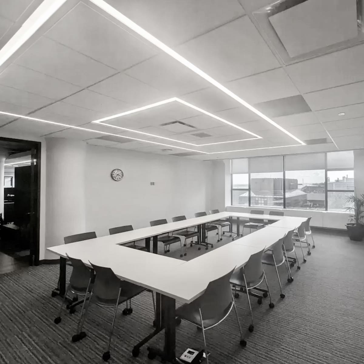 A modern conference room with a long table surrounded by chairs, large windows, and overhead lighting.