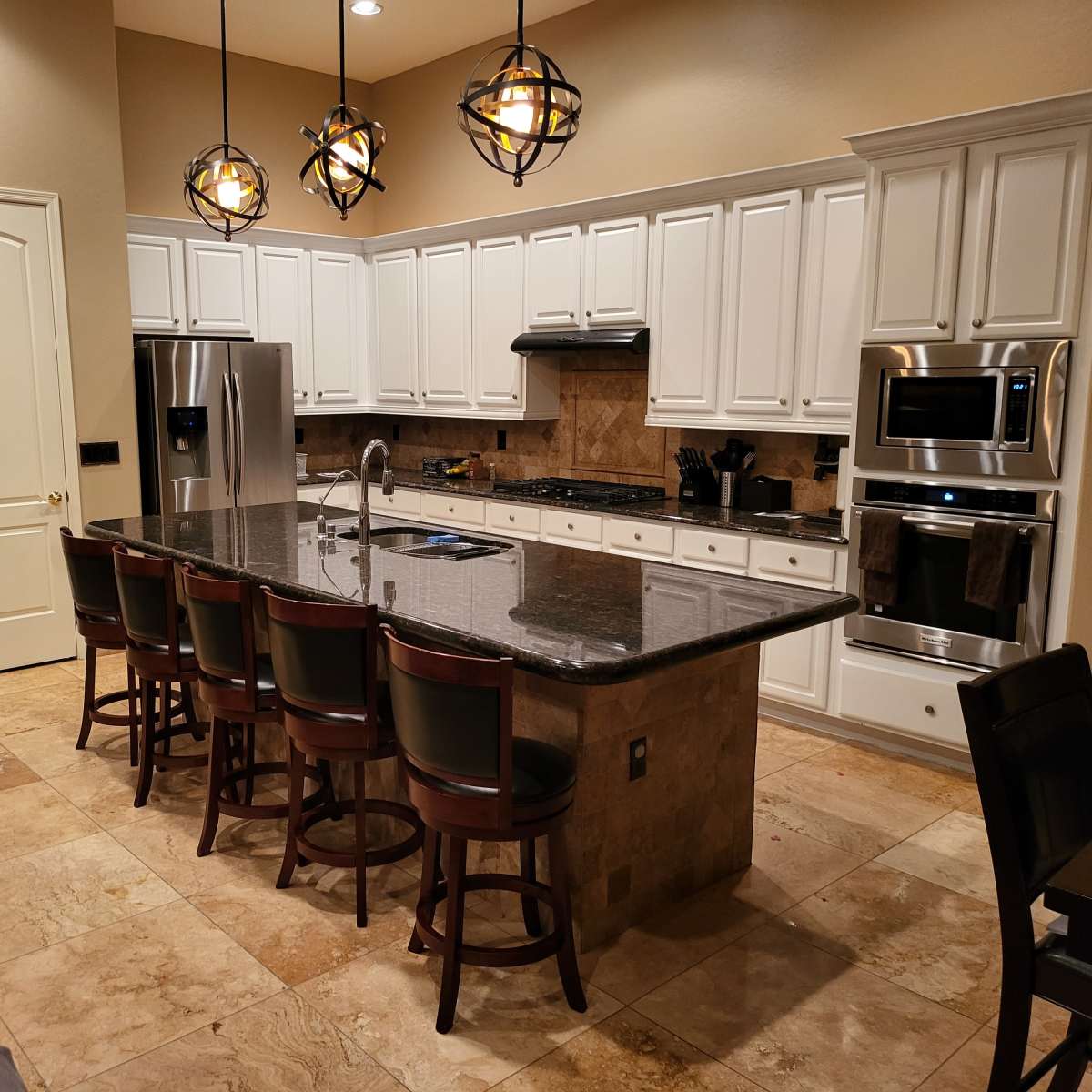 A modern kitchen with white cabinetry, a large granite island with seating for eight, and stainless steel appliances.