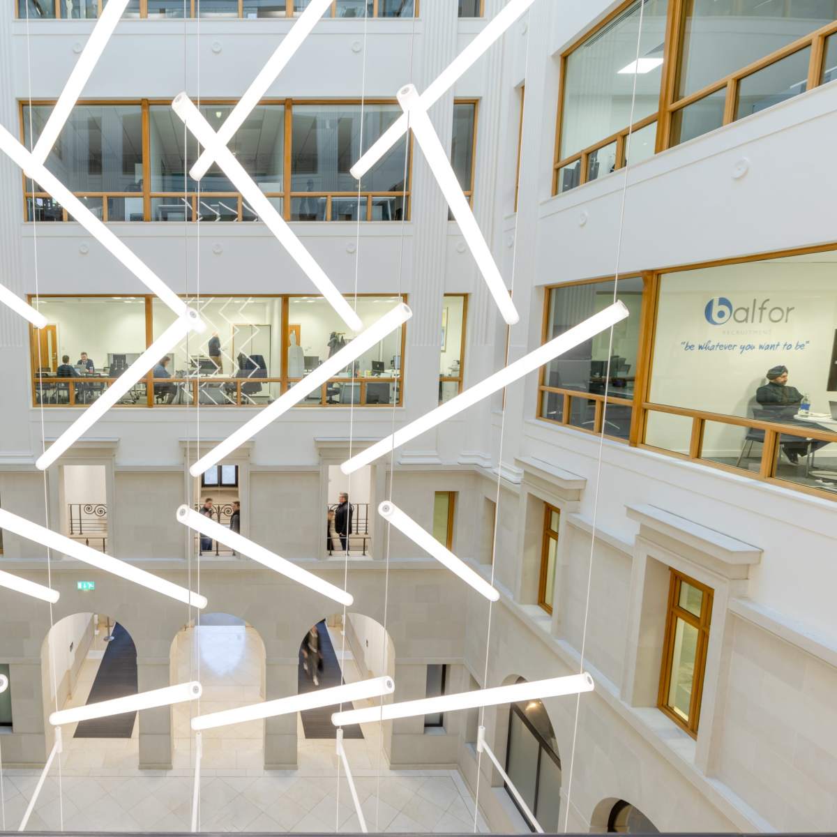 An interior view of a modern multi-level building with angular light fixtures suspended from the ceiling and several people visible in the background.