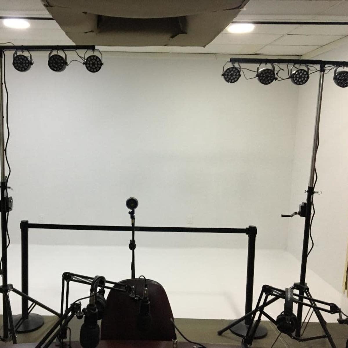 A bare studio space with a white backdrop, lighting stands equipped with multiple lights, and a microphone setup on a table.
