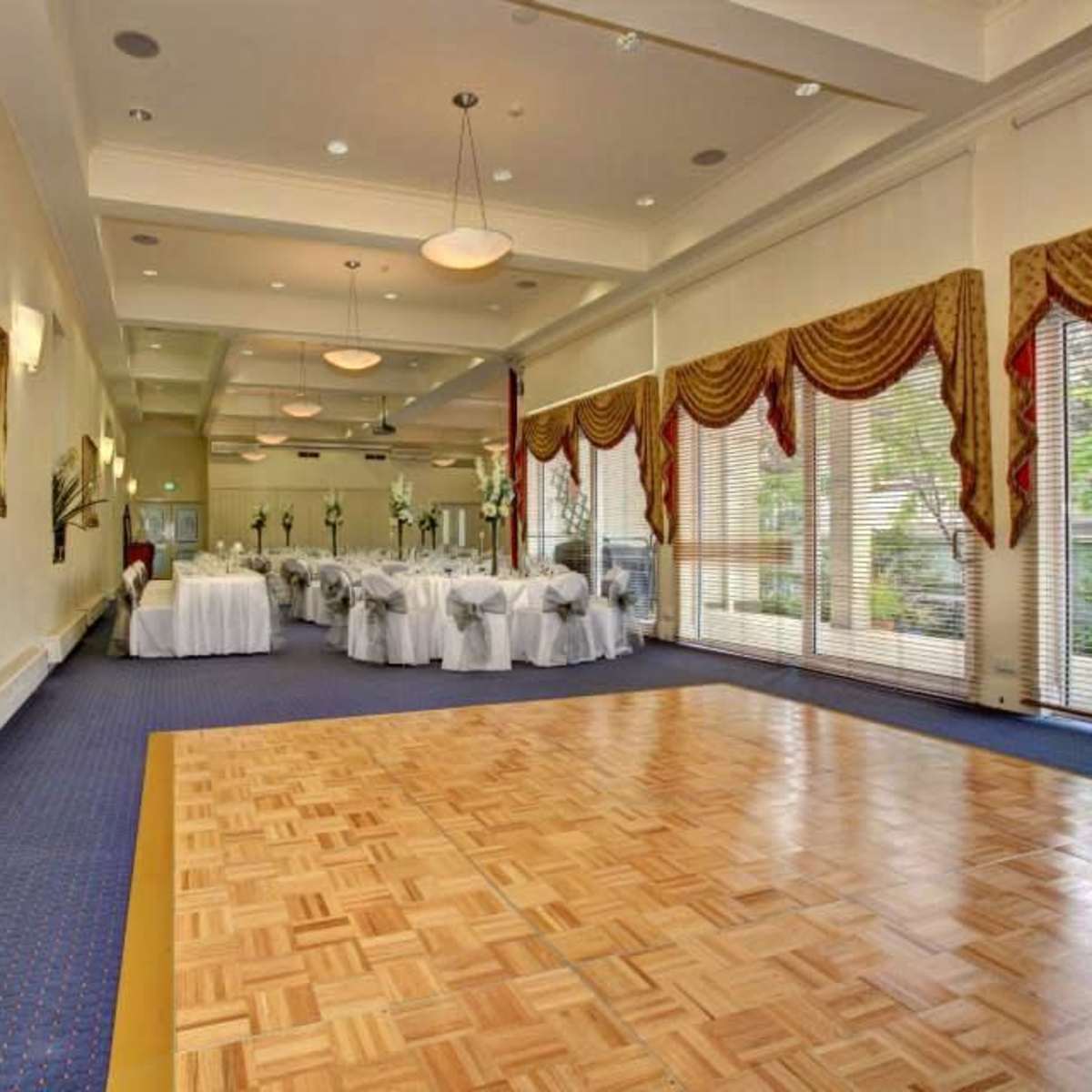 A spacious banquet hall features a wooden dance floor and rows of elegantly set tables with white linens.