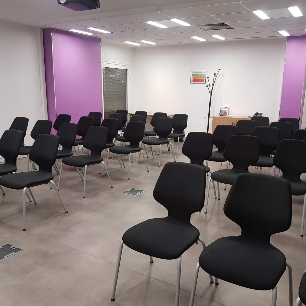 A seminar room with rows of black chairs arranged on a tiled floor, accented by purple walls.