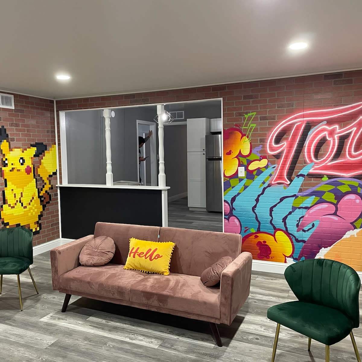 A modern living space with a pink sofa, green chairs, and vibrant wall murals featuring a Pikachu and colorful graffiti.