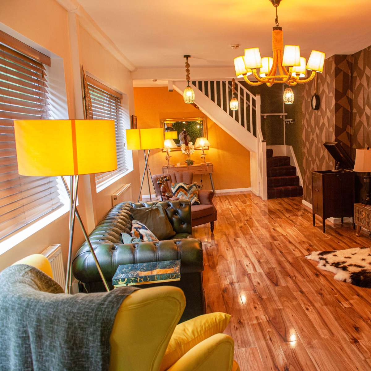 A spacious living room featuring a mix of leather and fabric seating, wooden flooring, and decorative wall patterns.