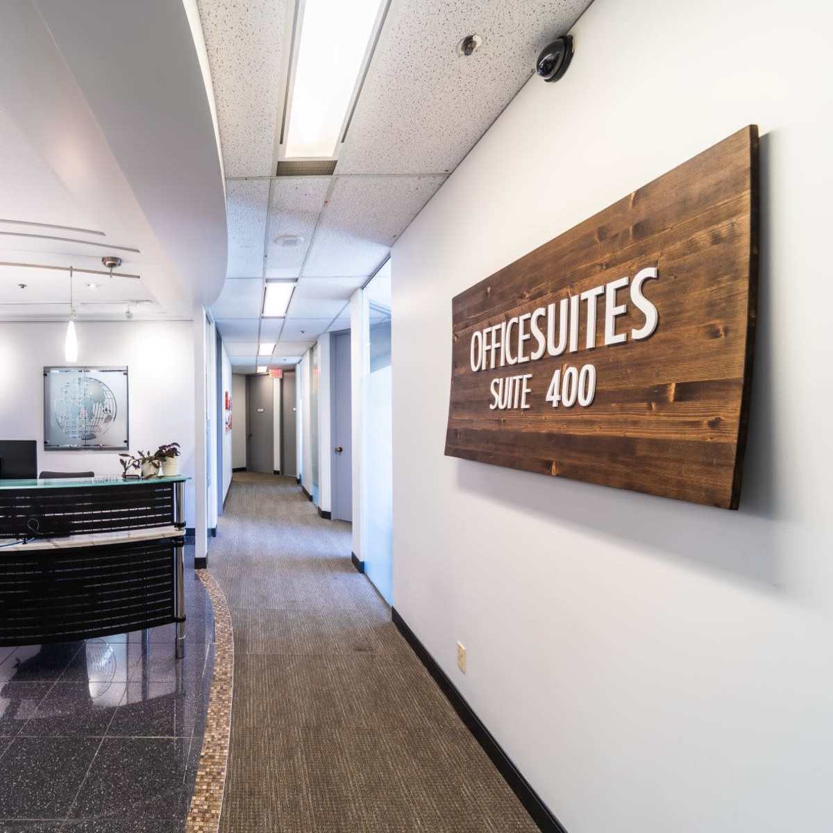 A modern office reception area with a curved front desk and a sign indicating "OFFICESUITES SUITE 400" on the wall.