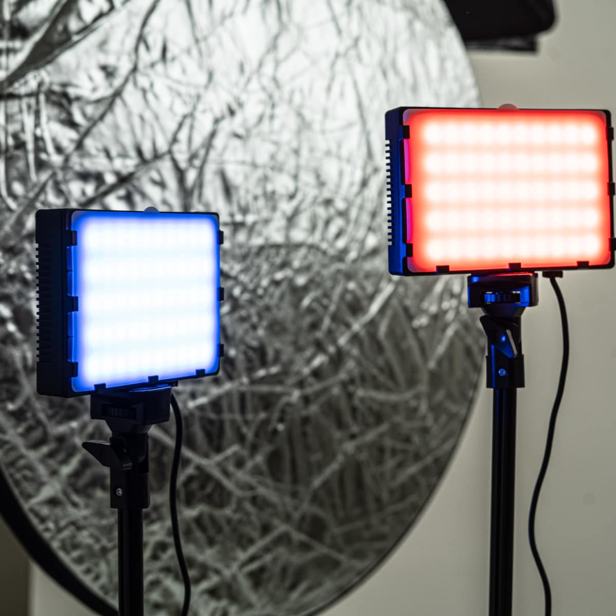 Two LED lights on stands, one emitting blue light and the other emitting red light, in front of a circular reflective surface.