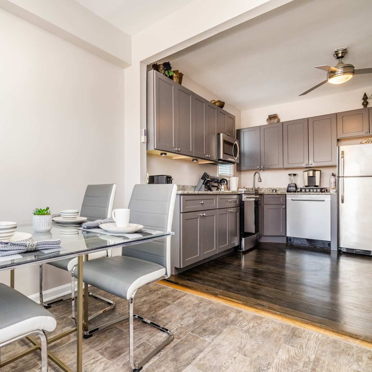 A modern kitchen features a dining table set for three, with gray chairs and a view of cabinetry and appliances in the background.