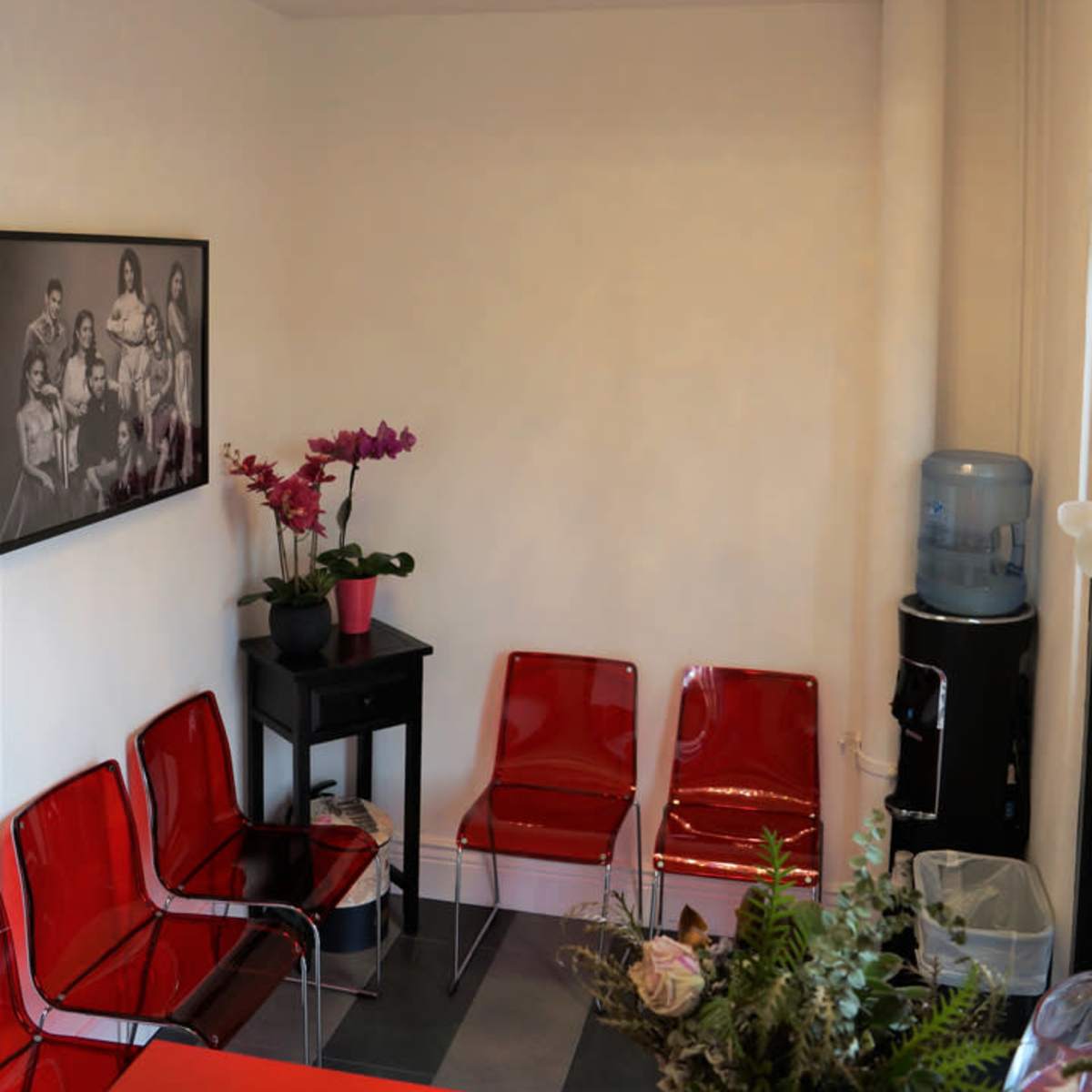 A waiting room with red chairs, a table holding a potted plant, a water cooler, and a decorative chandelier overhead.