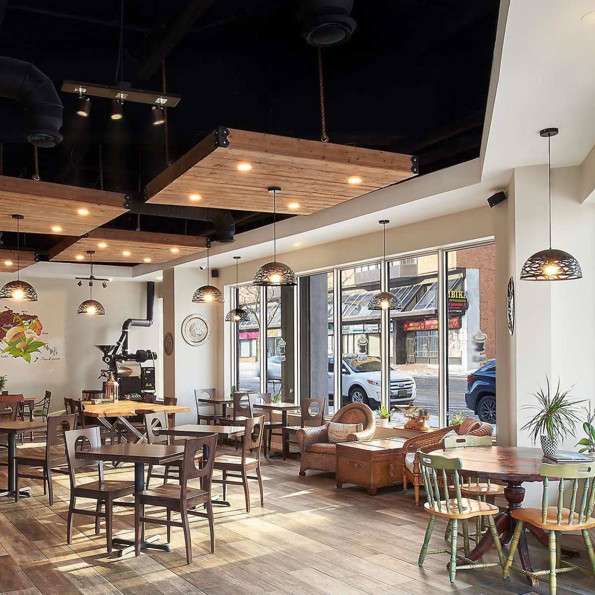 A modern restaurant with wooden decor, tables, and chairs, illuminated by pendant lights, and large windows overlooking a street.